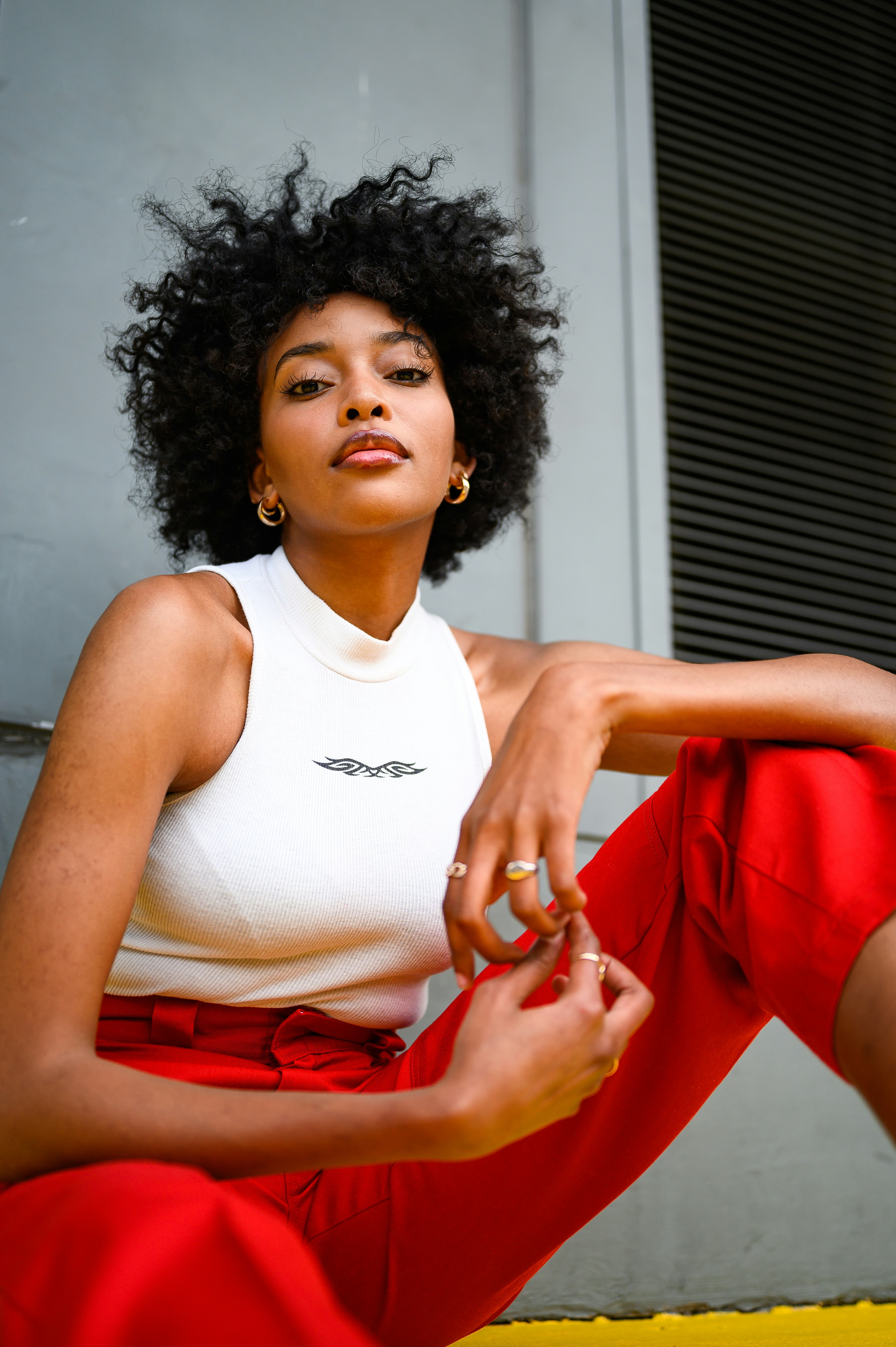 Tessa’s reference photo, with short dark curls, gold hoop earrings, a white sleeveless top, and red trousers